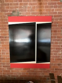 a black and red painting hanging on a brick wall